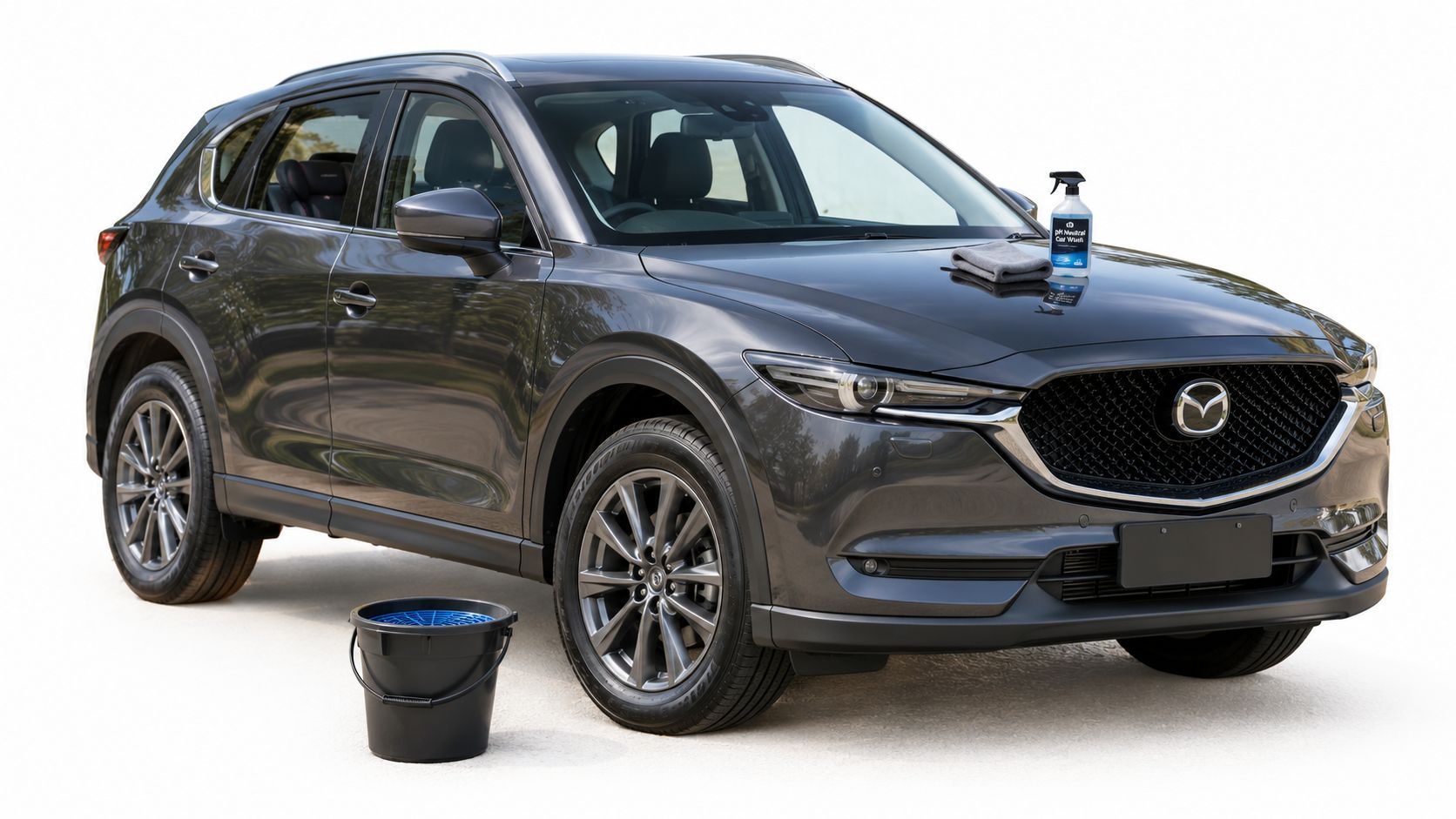A charcoal grey Mazda SUV parked outdoors with a car wash spray bottle and microfiber towel nearby.