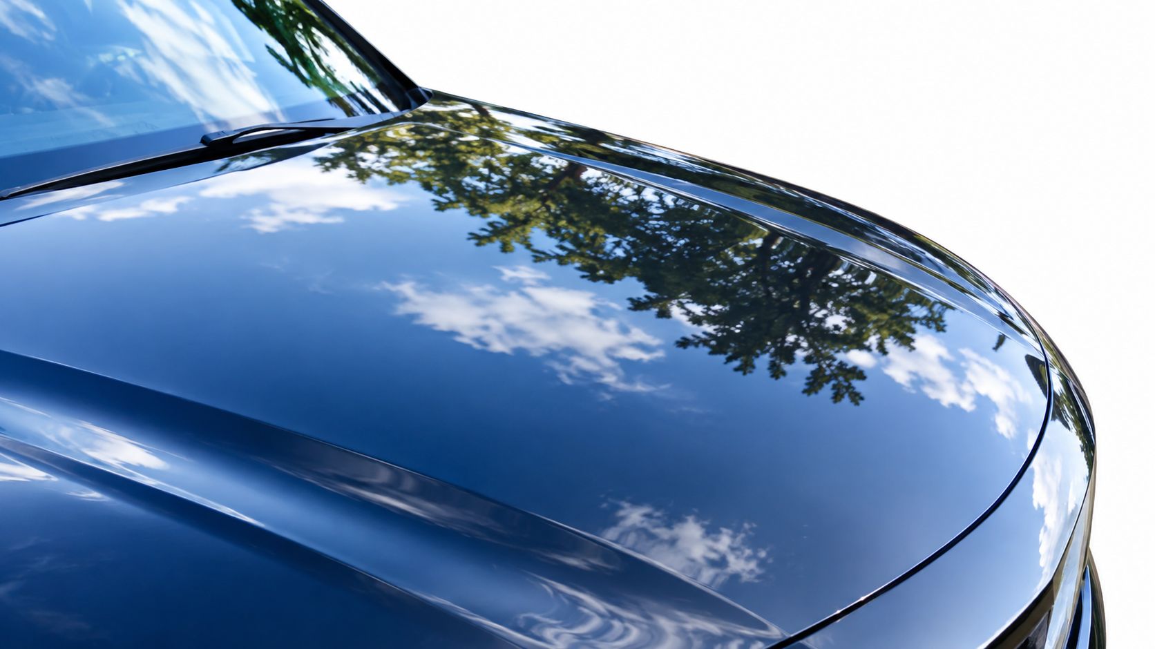 Close-up of a glossy, reflective dark car hood showing a clear blue sky and tree reflection.