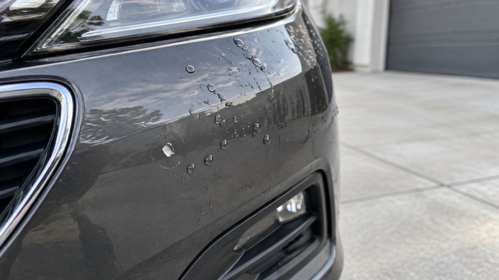 Close-up of a car bumper with a noticeable paint chip next to water beads on surface