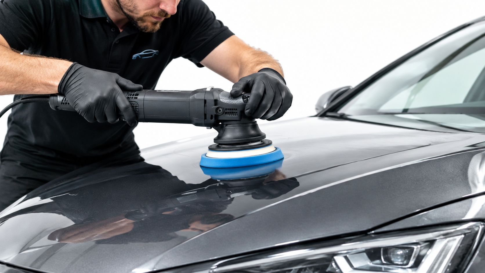 A professional car detailer uses a dual action polisher to buff and restore a grey car hood.