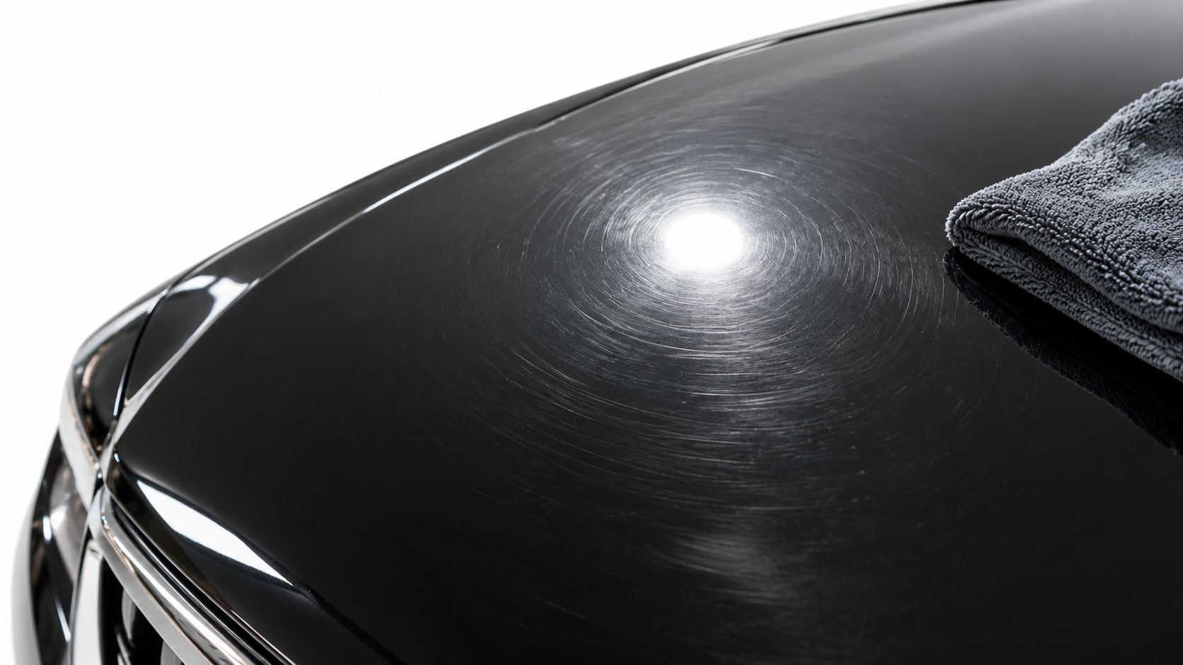 A close-up view of a black car hood showing swirl marks and scratches with a microfiber cloth.