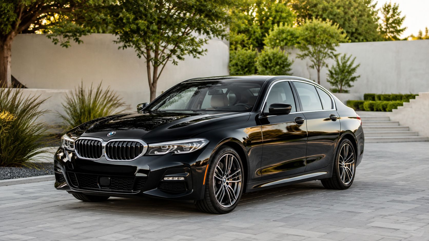 A sleek black BMW 3 Series sedan parked on a stone paved driveway surrounded by landscaping.
