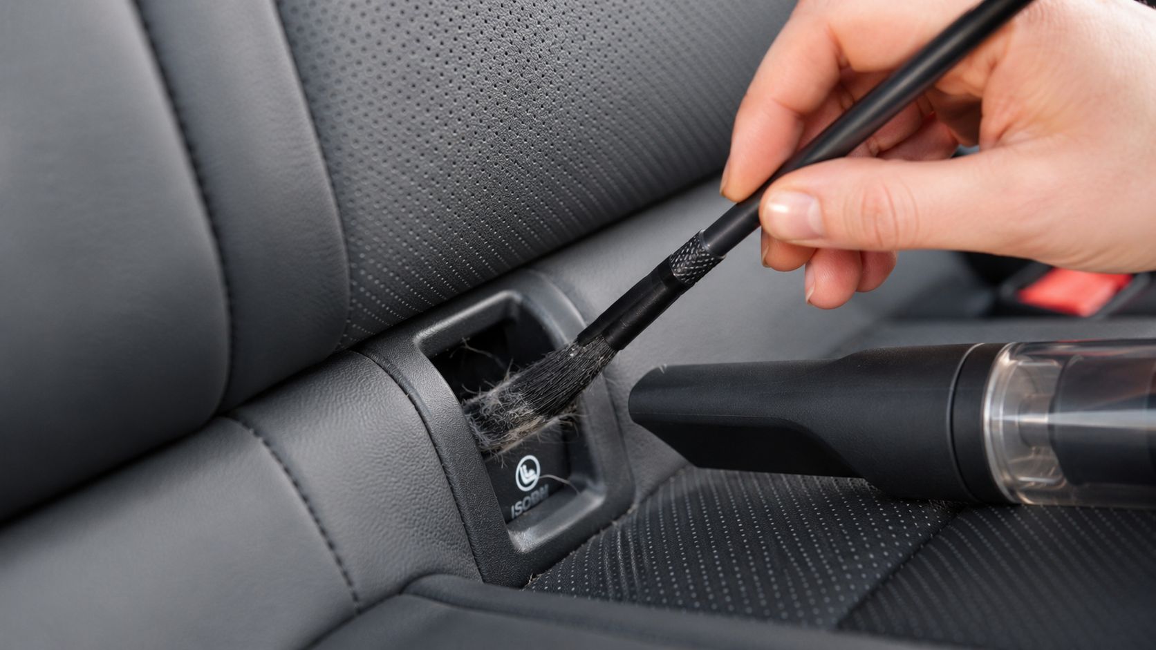 A person uses a cleaning brush to remove pet hair from the car seat ISOFIX anchor point.